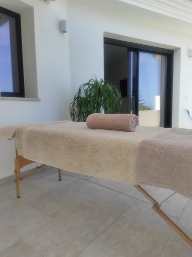 Mesa de masaje con una toalla enrollada, situada en un entorno luminoso y moderno.