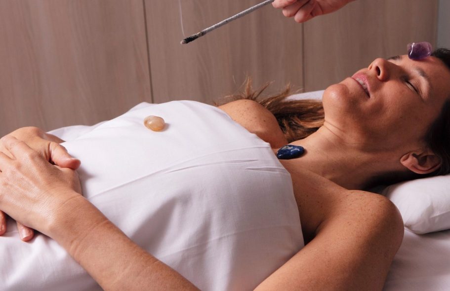 Woman receiving a facial treatment, lying down and relaxed, with stones on her skin.