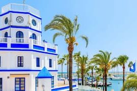 Estepona Marina. White and blue building with palm trees and marina in the background