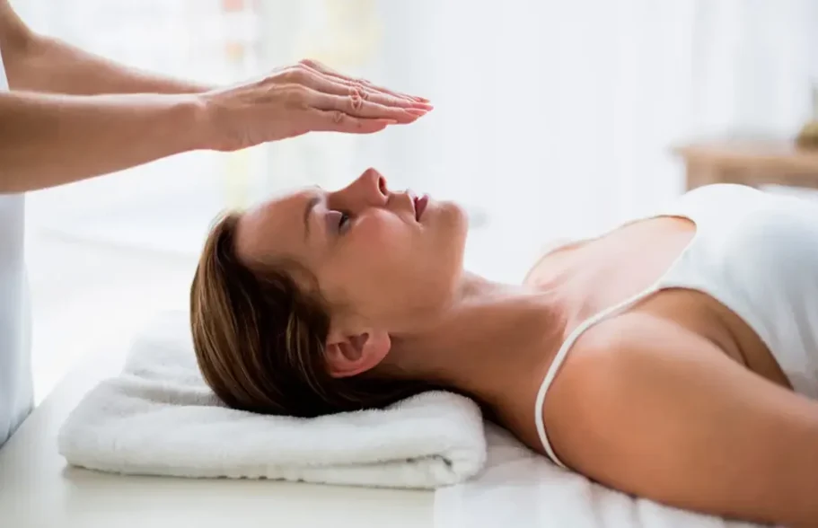 Woman in relaxation position receiving a treatment, with hands on her forehead.