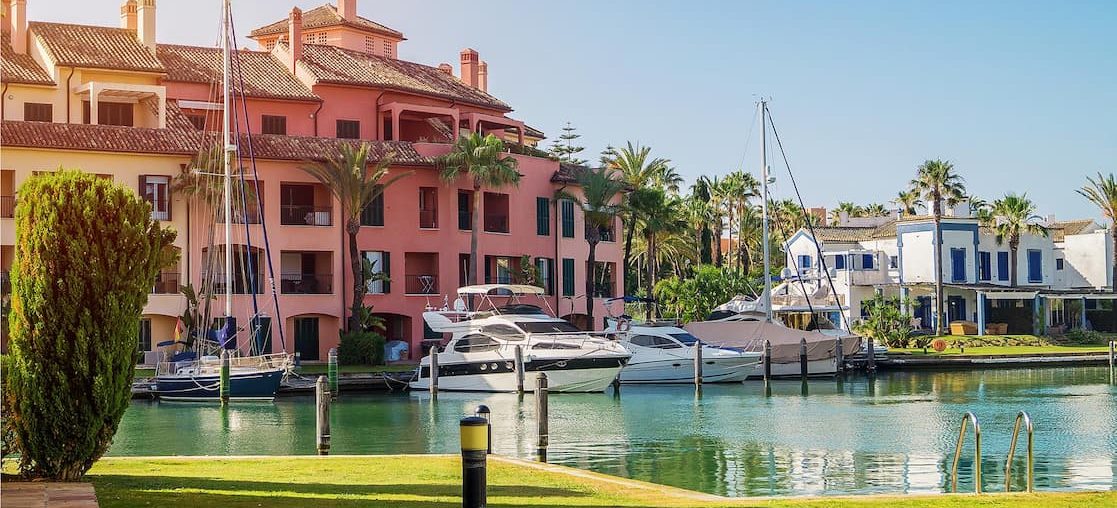 Exclusive Massage at home in Sotogrande Sotogrande Marina with colourful boats and buildings surrounded by palm trees.