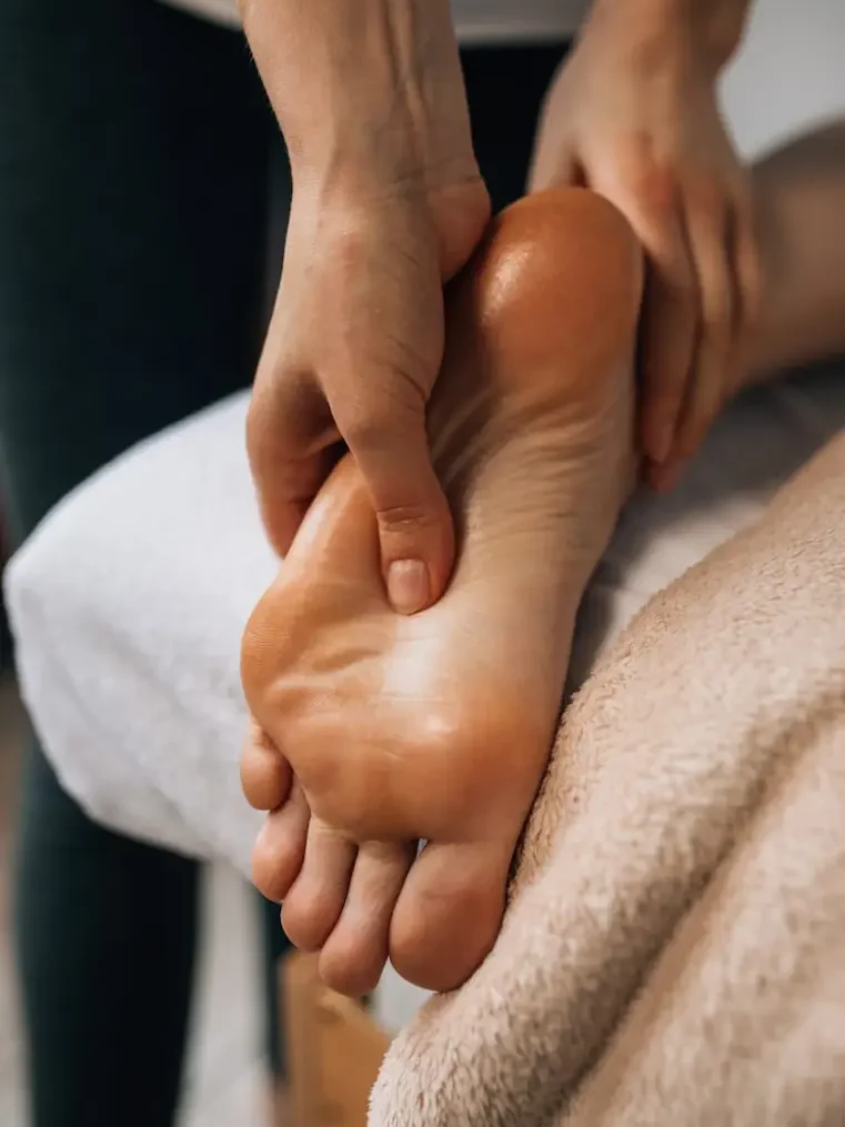 Massage on one foot, with hands gently applying pressure and lighted candles in the background.