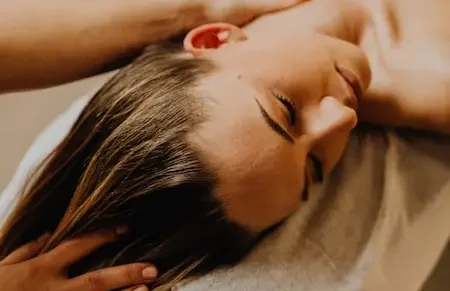Woman receiving a Relaxing massage at home, with her eyes closed and a hand on her neck.
