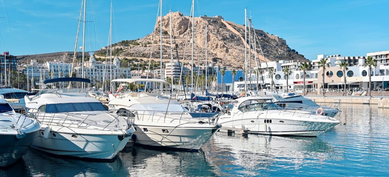 Puerto Banús with yachts, white buildings and mountains in the background under a clear sky.