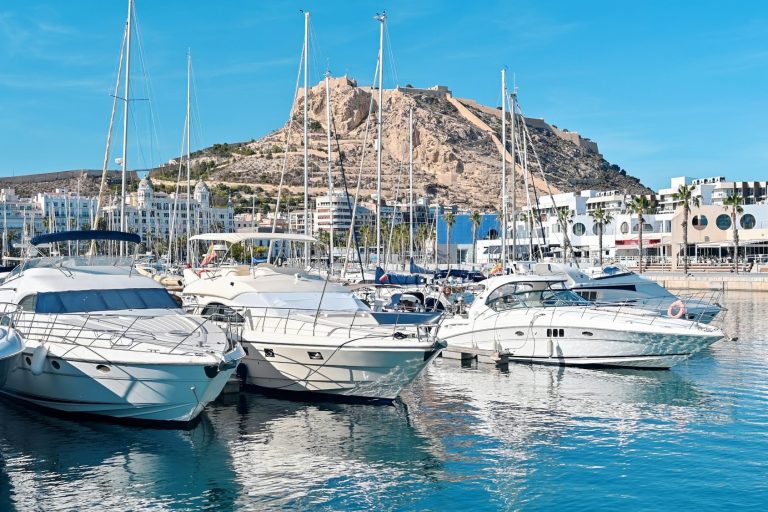 Sailboats lined up in Puerto Banús, with a mountain in the background and a blue sky. Book your perfect in-home massage with SENSE8