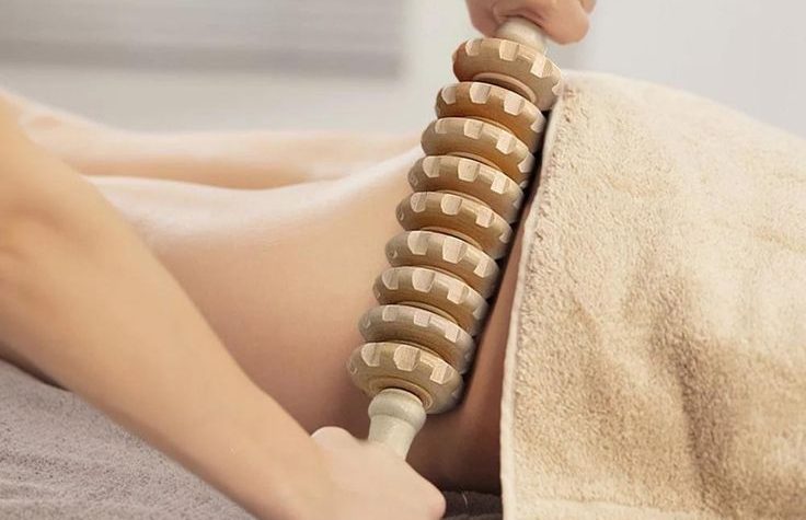 A person is massaged with a wooden roller on the lower back.