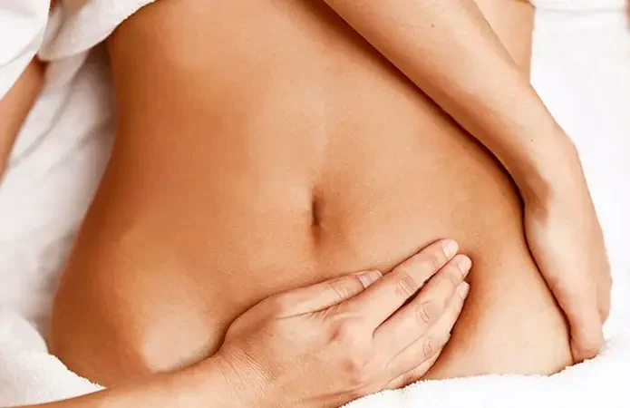 Hand caressing a bare abdomen on a smooth, light surface.