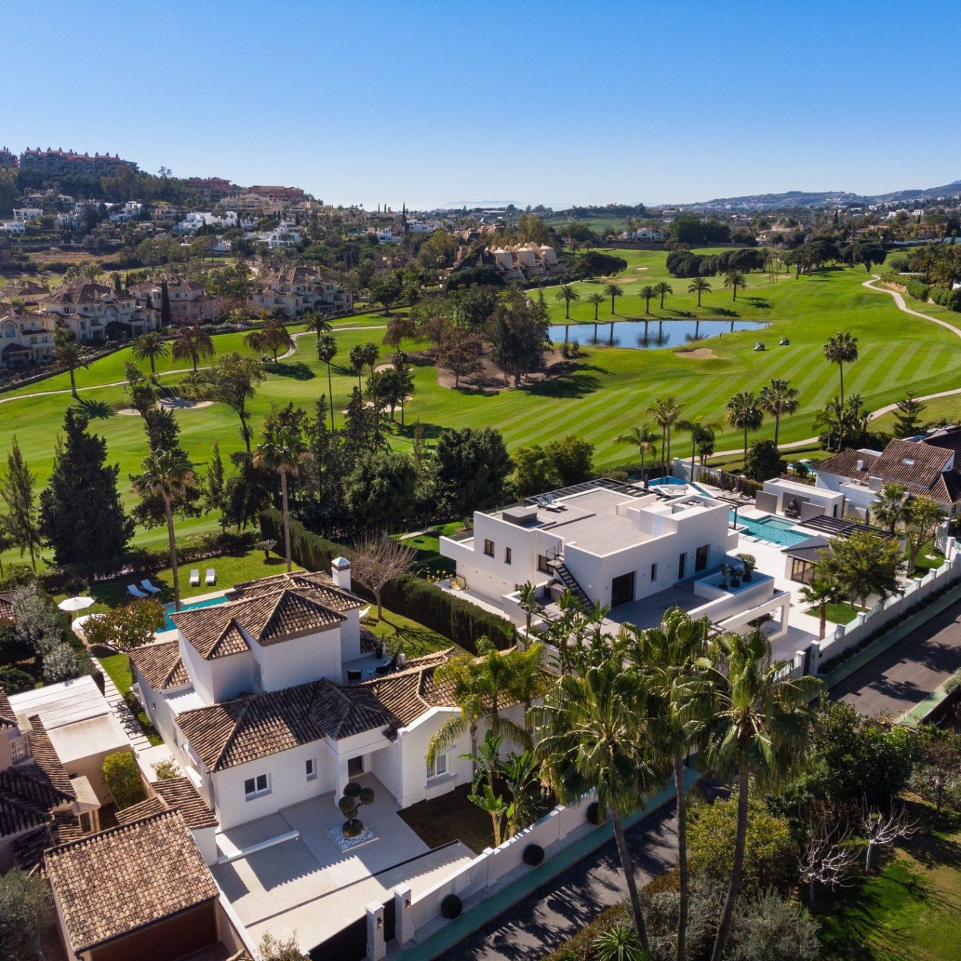Aerial view of a modern villa next to a golf course and green areas.