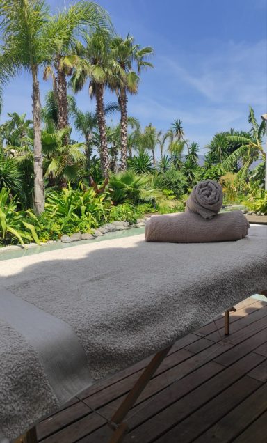 Outdoor massage table with rolled towel, surrounded by palm trees and vegetation.