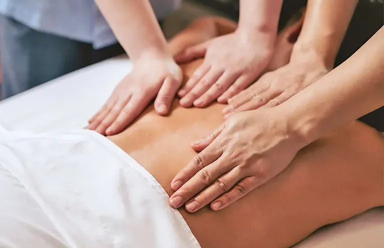 Three hands massage the back of a person lying down.