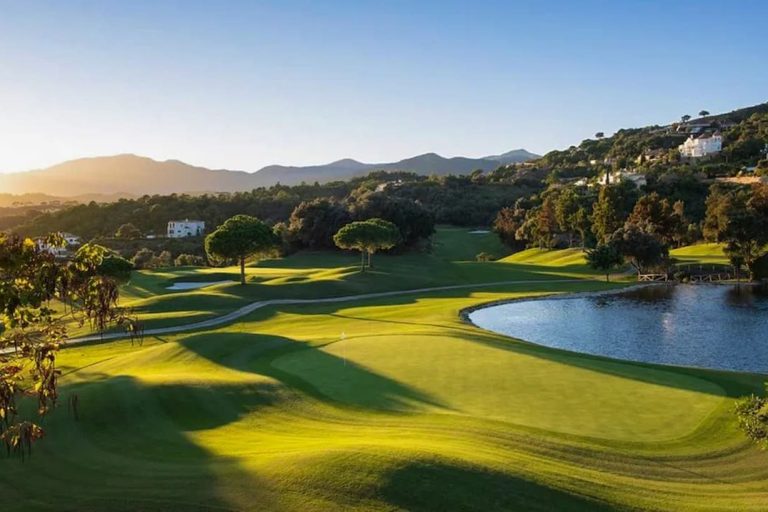 A golf course at dawn, with trees and a lake, surrounded by hills in Marbella