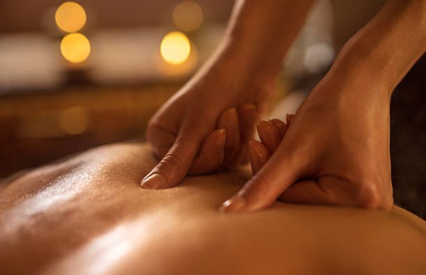 Hands massaging a person's back with diffuse lights in the background.