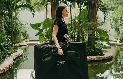 Woman with a large black bag, surrounded by plants and water in a natural setting.