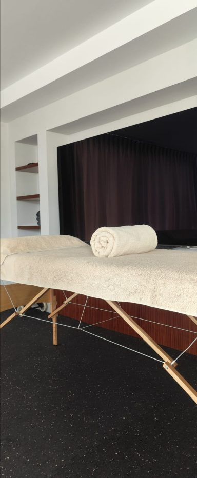 Beige massage table against a background of shelves and curtains.