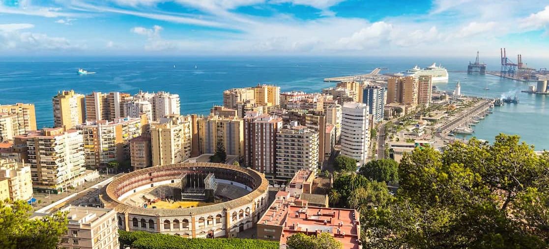 Panoramic view of the Malaga coastline with buildings and a stadium on the seafront.
