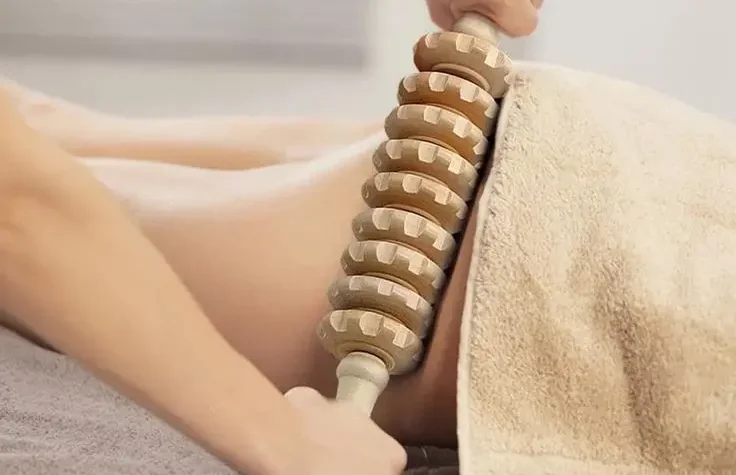 A person is massaged with a wooden roller on the lower back.
