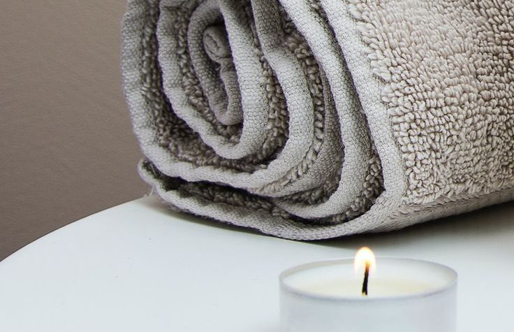 A rolled-up towel next to a lit candle on a white surface.