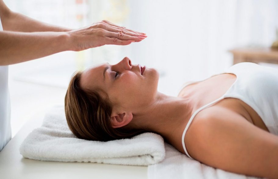 Woman in relaxation position receiving a treatment, with hands on her forehead.