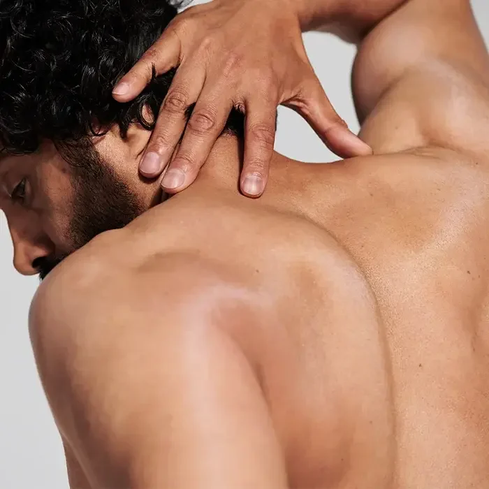 Man on his back, touching his neck, with brown skin and curly hair.