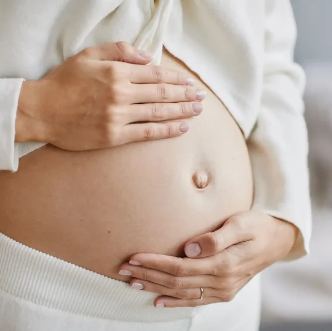 Pregnant belly with hands caressing it, in a bright and cozy environment.