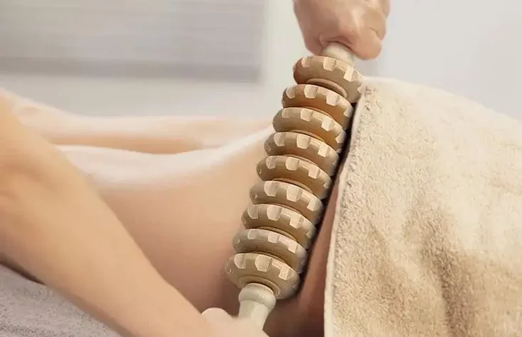 A person is massaged with a wooden roller on the lower back.