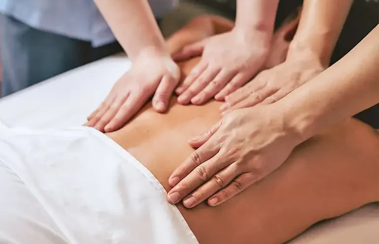 Three hands massage the back of a person lying down.