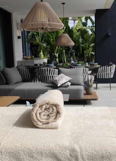 Rolled towel on a table, with a modern living room background and tropical plants.