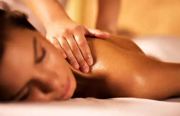 Hands massaging a person's back with diffuse lights in the background.
