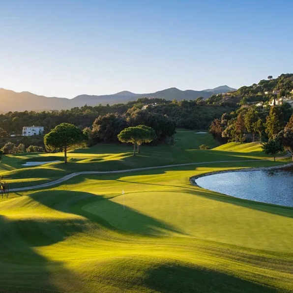 Golf course landscape with mountains in the background and a reflecting lake.