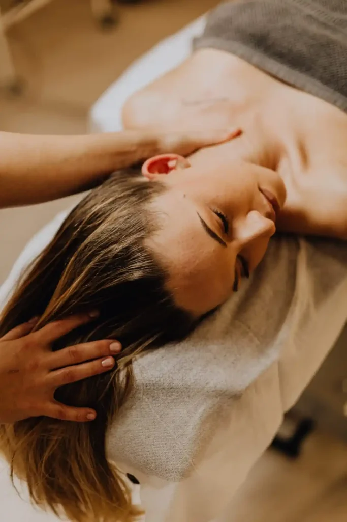 Woman receiving a massage on a treatment table, with hands on her head.
